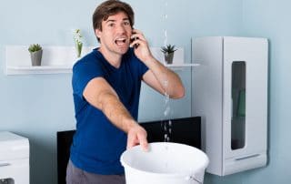 Man on a phone holding a bucket under leaking ceiling