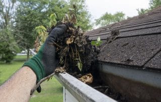 Hands Cleaning Gutters Filled With Leaves and Sticks