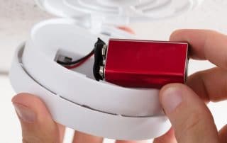Close-up Of A Person's Hand Inserting Battery In Smoke Detector