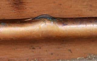 frozen and cracked copper water pipe with ice pushing out of the crack