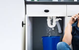 Woman talking on a phone in front of a leaking sink drain