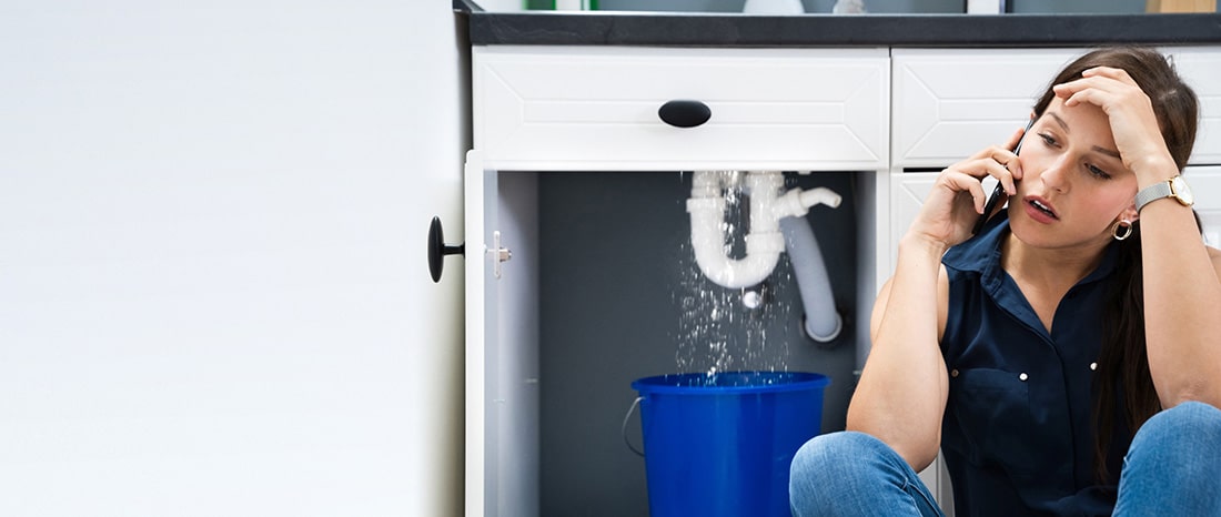 Woman talking on a phone in front of a leaking sink drain