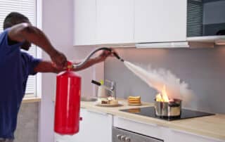 Man putting out a fire in a kitchen with a fire extinguisher